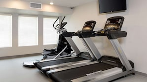 A gym with two treadmills, a stationary bike, and a TV mounted on the wall. - WoodSpring Suites Houston IAH Airport (Humble)