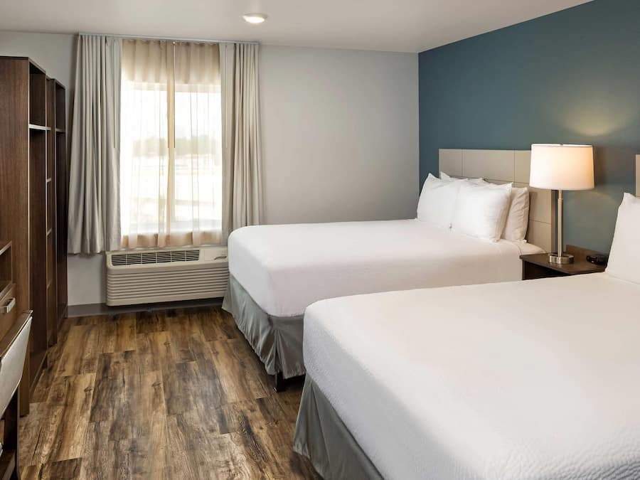 Une chambre d’hôtel avec deux lits, une télévision, une fenêtre avec des rideaux, une lampe de chevet et un plancher en bois.