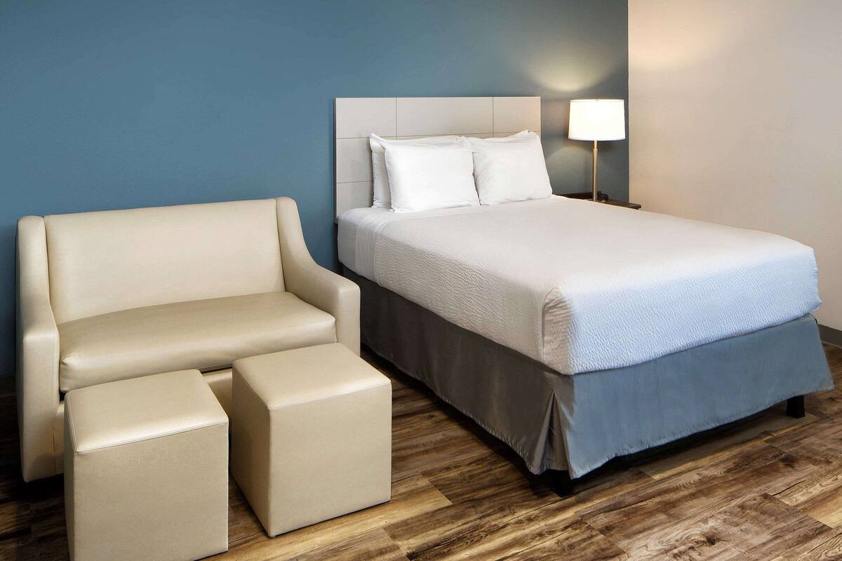 A hotel room with a bed, a sofa, and a nightstand with a lamp.