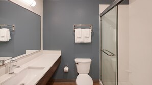 A modern bathroom with a large mirror, two sinks, a toilet, and a glass shower enclosure. - WoodSpring Suites Houston IAH Airport (Humble)