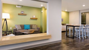 A modern living room with a sofa, coffee table, and a dining area with chairs and a table. - WoodSpring Suites Houston IAH Airport (Humble)