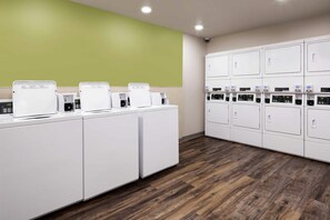 A laundry facility with multiple washing machines and dryers, wooden flooring, and a green wall. - WoodSpring Suites Houston IAH Airport (Humble)