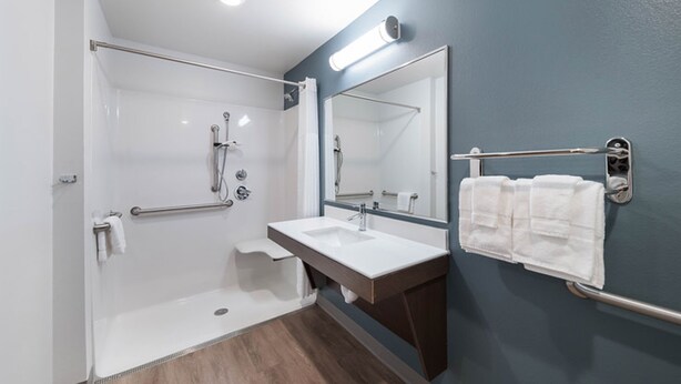 A modern bathroom with a walk-in shower, a sink, and a large mirror. - WoodSpring Suites Houston IAH Airport (Humble)