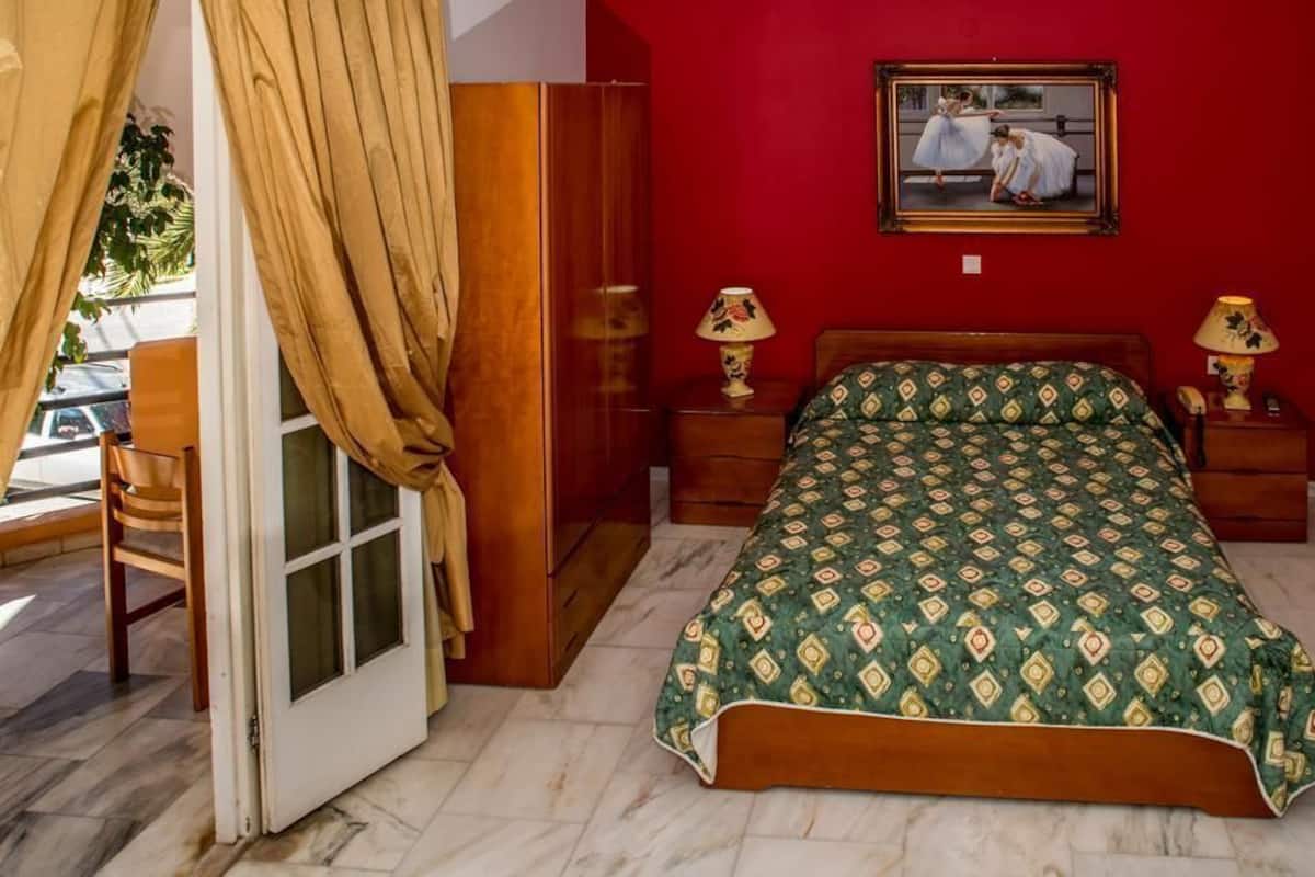 Un dormitorio con cama, dos mesitas de noche con lámparas, un armario de madera, una pared roja y una ventana con cortinas.