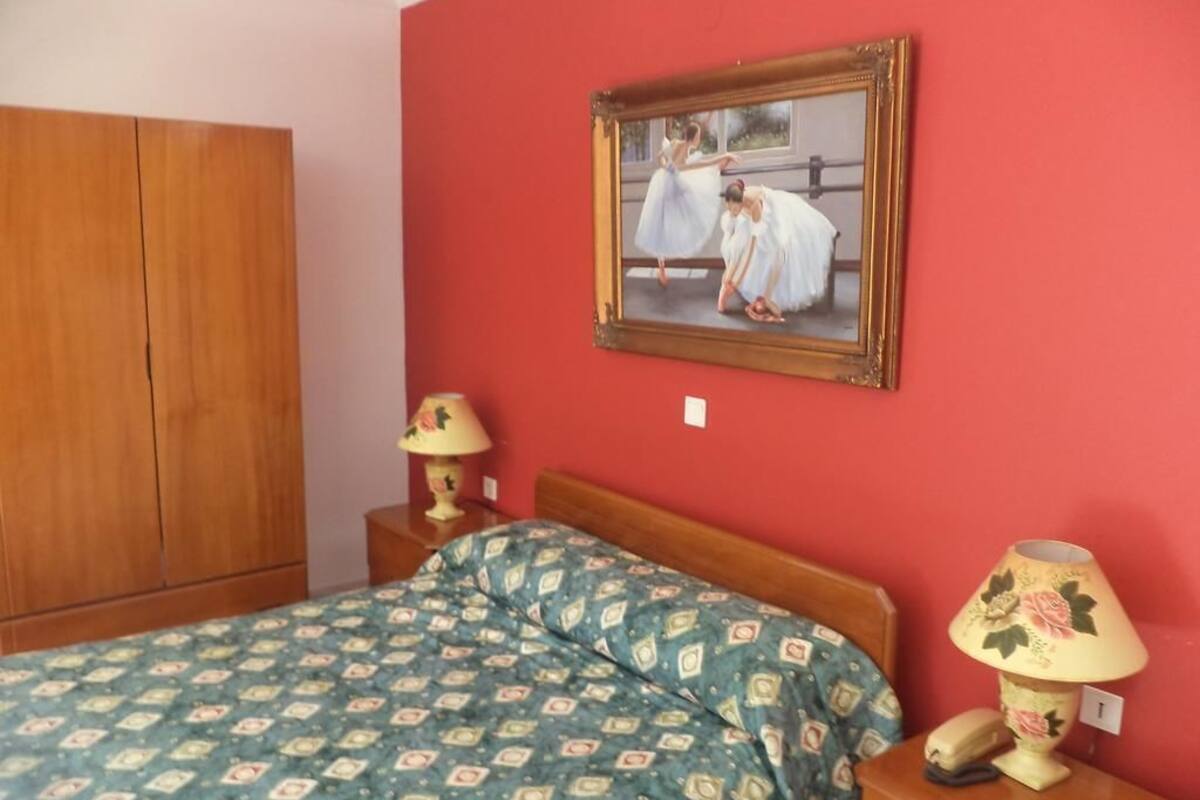 Un dormitorio con un armario de madera, una colcha estampada, un cuadro de bailarinas y dos lámparas de noche.