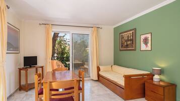 A room with a dining table, chairs, a sofa bed, a TV, and a small cabinet.