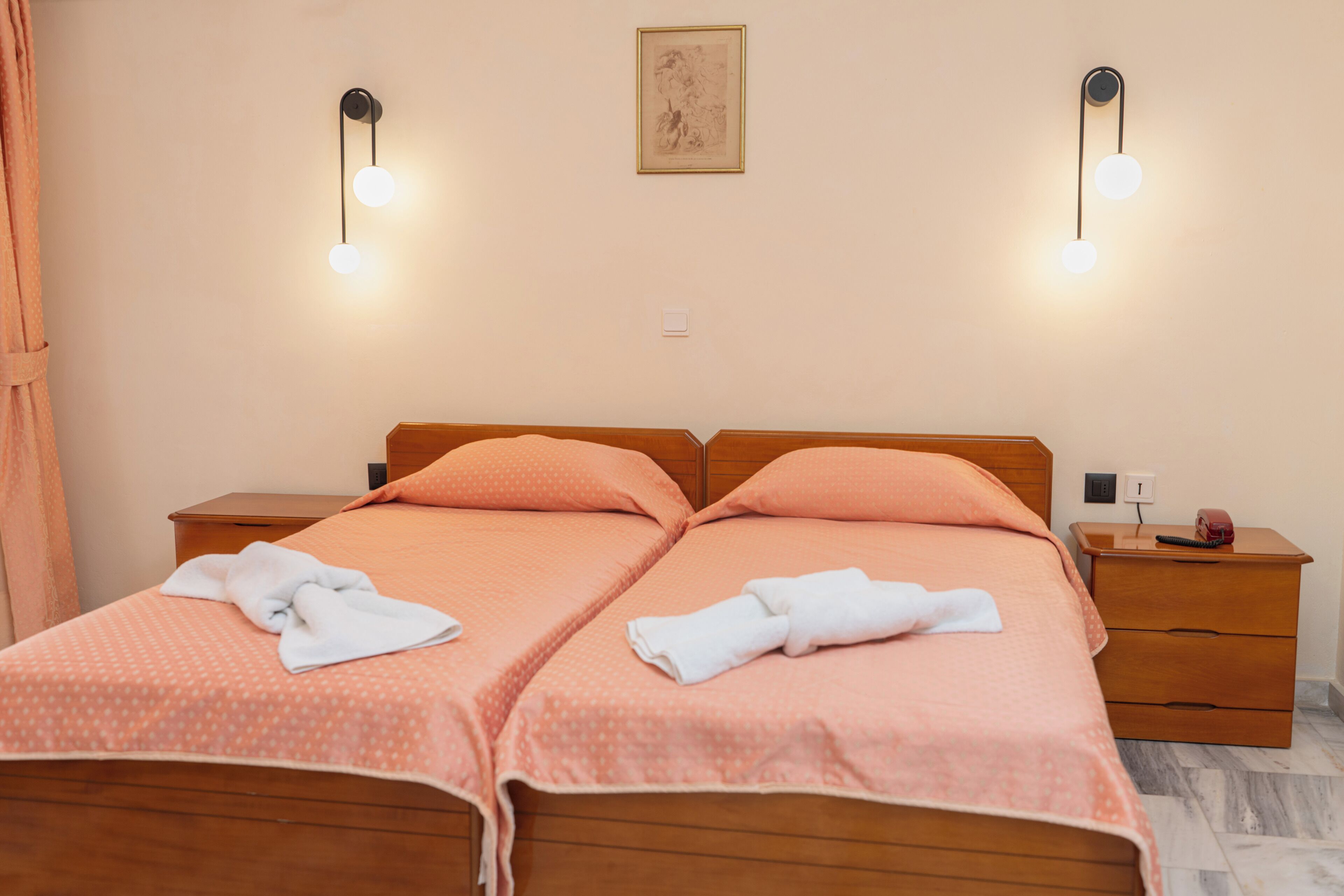 Una cama doble con almohadas a juego y una toalla doblada con cuidado, una mesita de noche de madera con lámpara, y un cuadro en la pared.