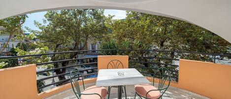 A balcony with a table and chairs, offering a view of trees and buildings.