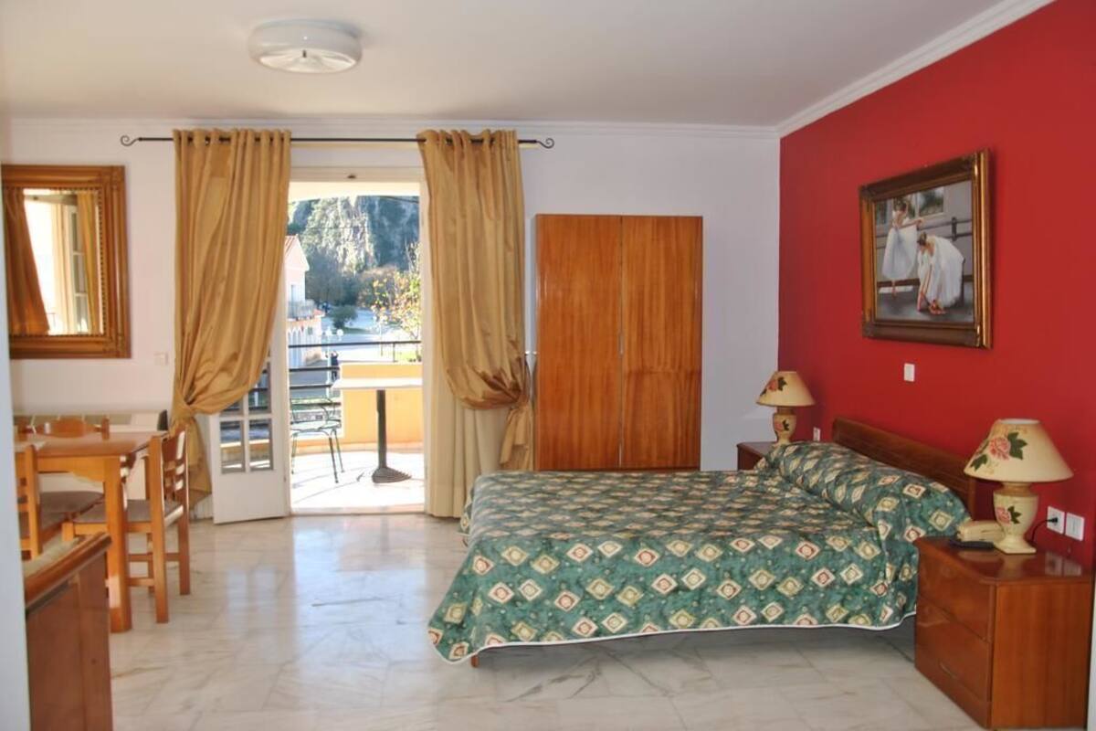 Un dormitorio con cama, escritorio, silla, ventana con cortinas y un cuadro en la pared.