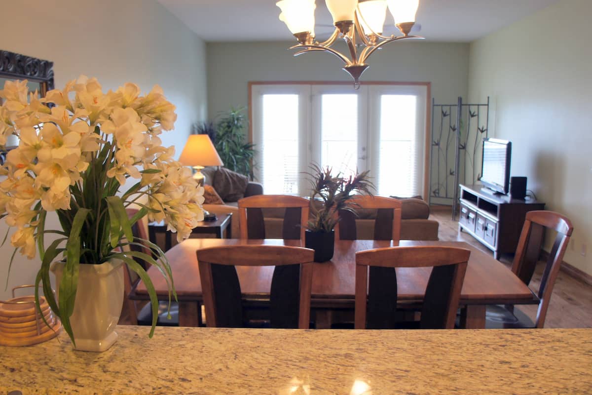 A dining area with a granite countertop, wooden dining table, and chairs. There is a vase with flowers on the countertop.