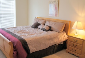 A neatly made bed with a floral bedspread and multiple pillows, a wooden nightstand with a lamp, and a framed picture on the wall. - Celebration Cove Table Rock Lakefront Condos (Branson)