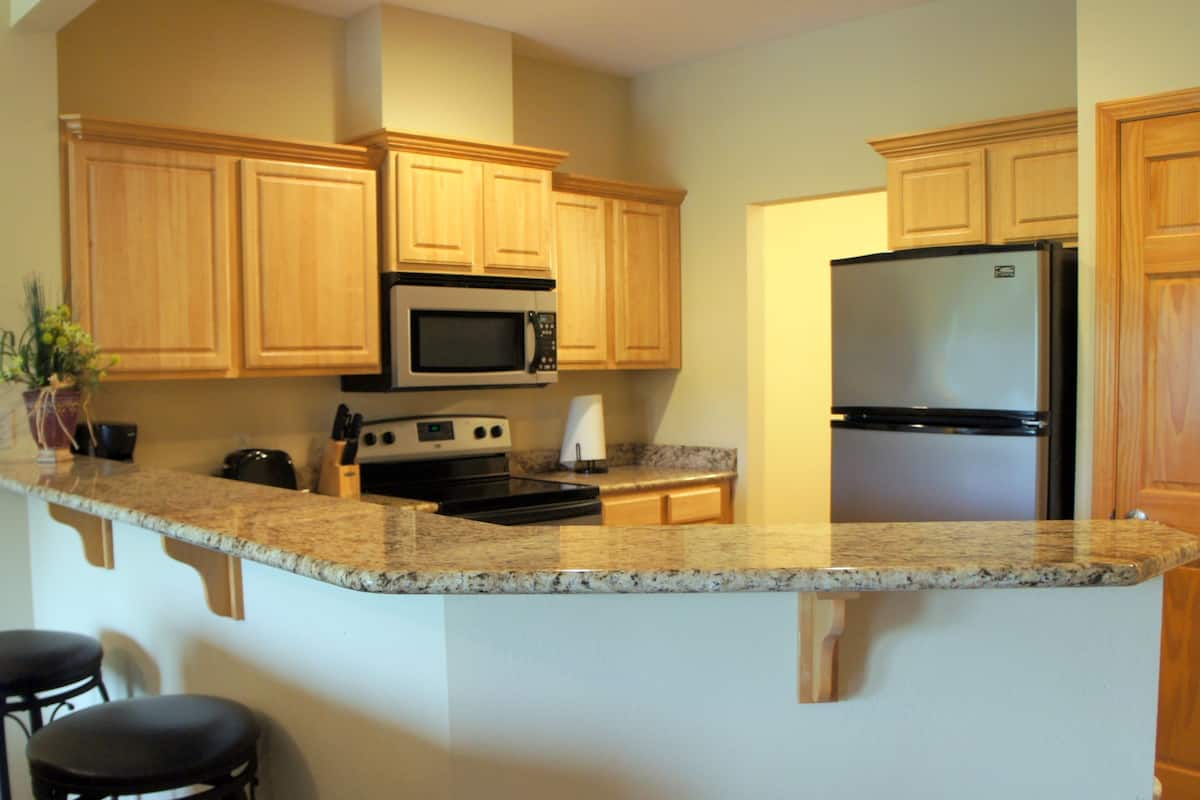 A kitchen with wooden cabinets, a granite countertop, a stainless steel refrigerator, a microwave, and a stove.