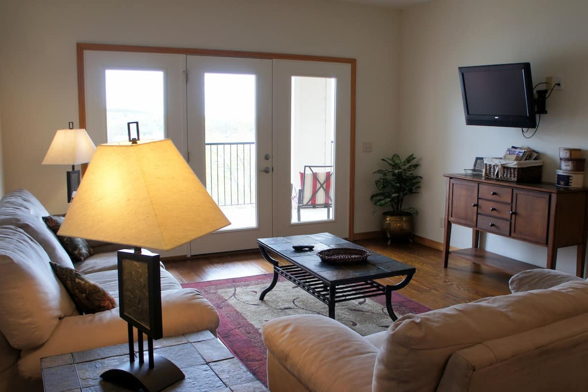 A living room with a sofa, a coffee table, a lamp, a television, and a sliding glass door leading to a balcony.