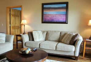 A living room with a beige sofa, a coffee table with decorative items, and a painting on the wall. - Celebration Cove Table Rock Lakefront Condos (Branson)