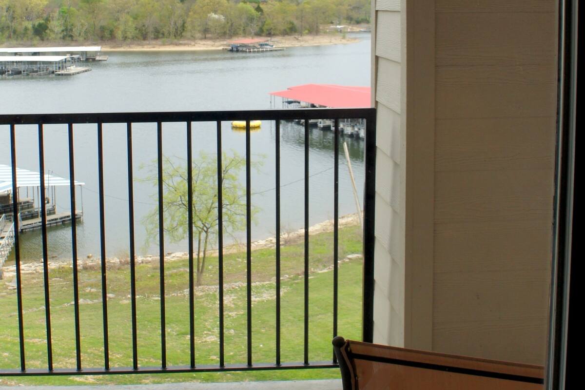 A balcony with a view of a lake, dock, and trees.