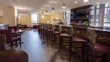 A bar area with multiple seating options, a television mounted on the wall, and a variety of bottles on the shelves.