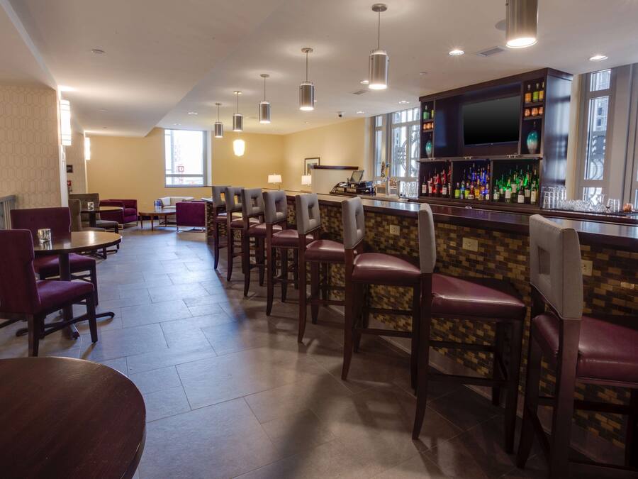 A bar area with multiple seating options, a television mounted on the wall, and a variety of bottles on the shelves.