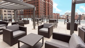 An outdoor patio area with wicker furniture and a view of city buildings. - Drury Plaza Hotel Pittsburgh Downtown (Pittsburgh)
