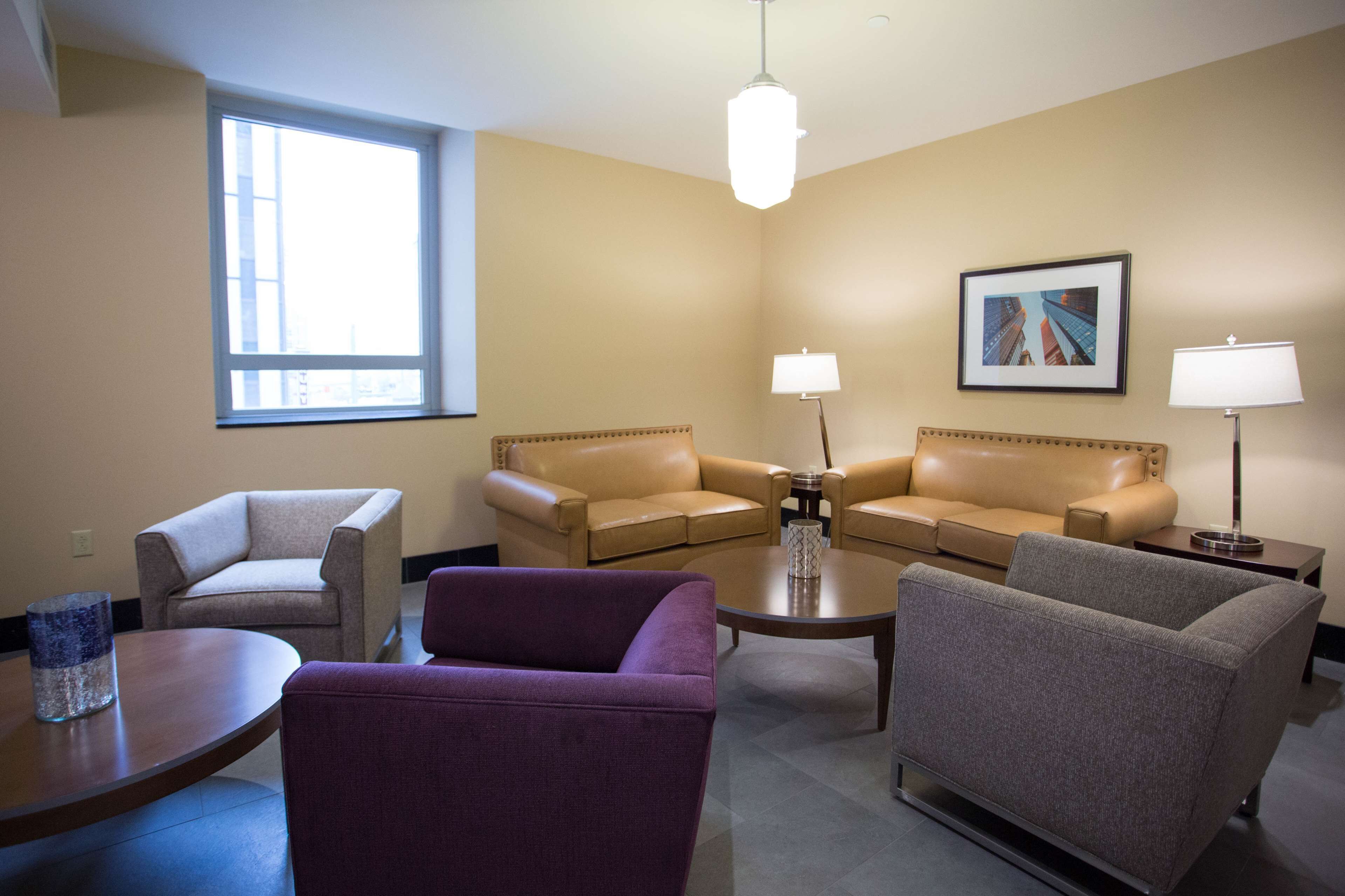 A hotel room with two beige sofas, a purple armchair, a small round table, and a floor lamp.