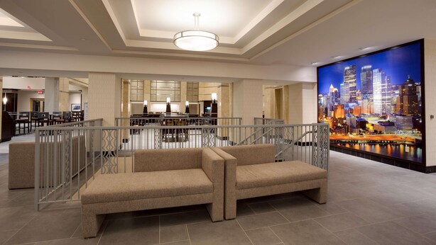 A spacious lobby with a high ceiling, a large cityscape mural, and a seating area with a railing. - Drury Plaza Hotel Pittsburgh Downtown (Pittsburgh)