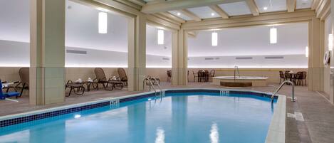 An indoor swimming pool with clear blue water, lounge chairs, and a sunlit ceiling.