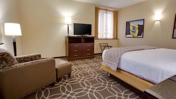 Une chambre d’hôtel avec un lit, un canapé, un téléviseur posé sur un meuble en bois et une moquette à motifs.