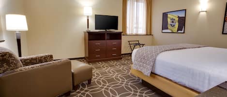 A hotel room with a bed, a sofa, a TV on a wooden cabinet, and a patterned carpet.