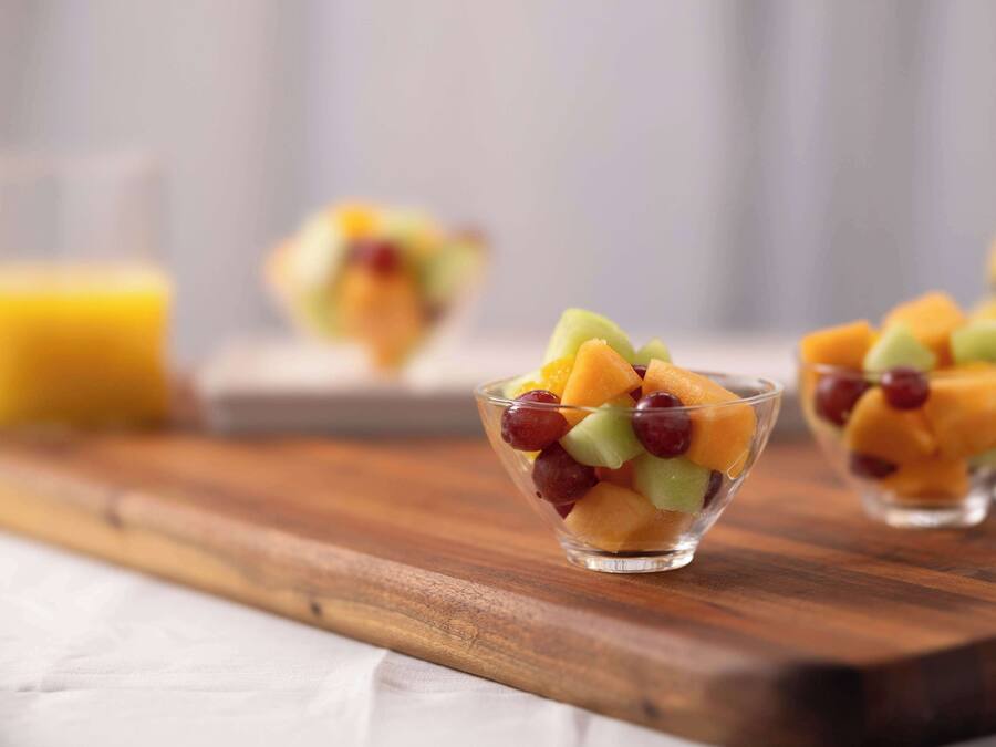 A wooden serving board with three clear glass bowls containing a fruit salad.