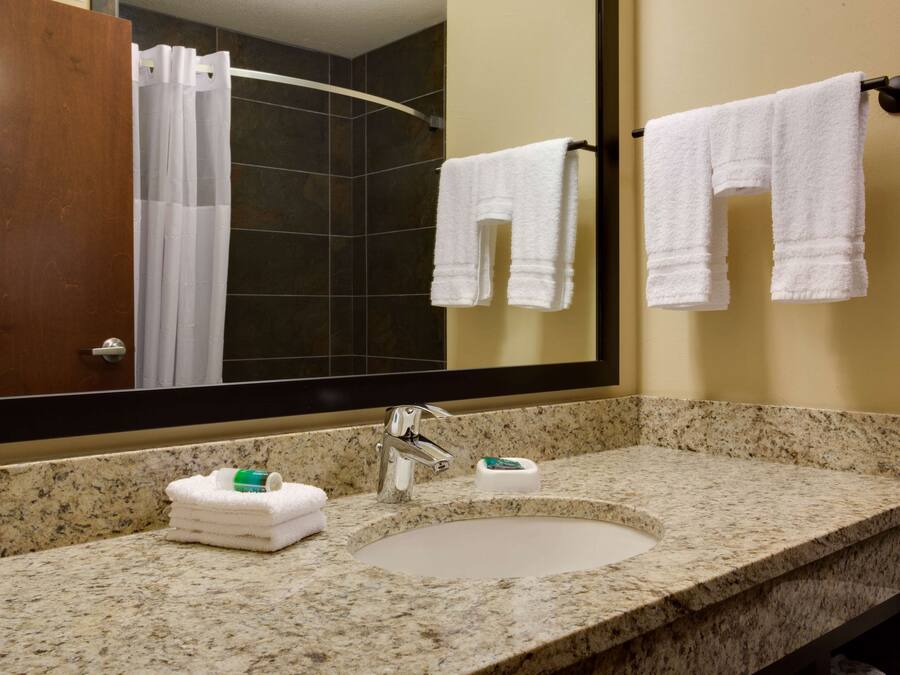 A bathroom with a granite countertop, a sink, a mirror, and two white towels hanging on a towel rack.