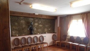 Una habitación con suelo de madera, una pared de piedra y una estatua. Varias sillas están dispuestas en filas.