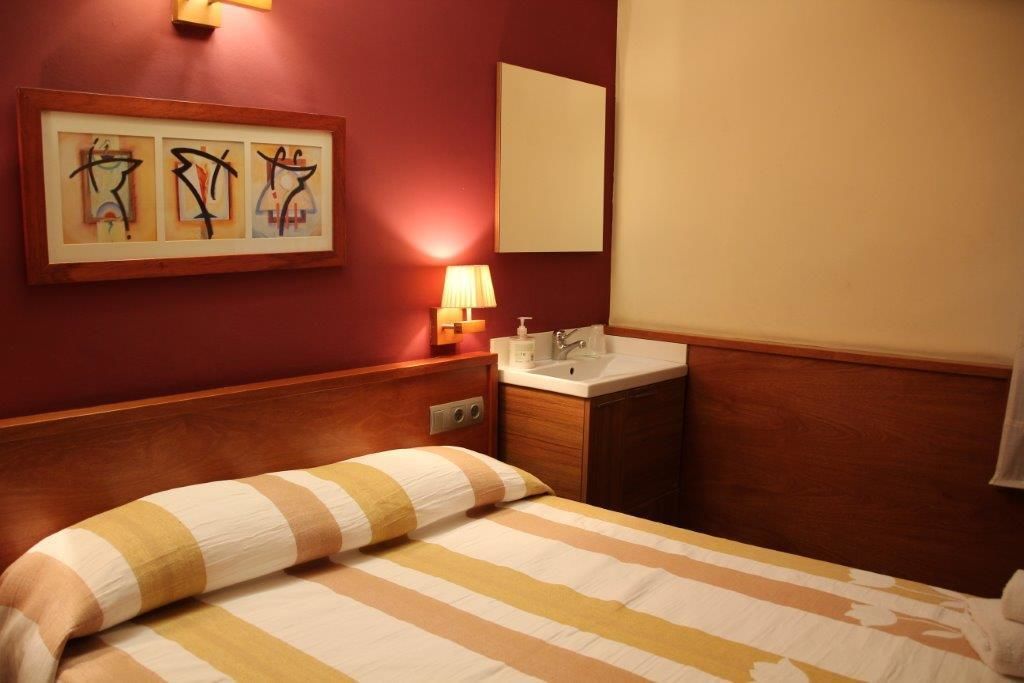 Hotelkamer met een bed, nachtkastje met lamp, spiegel en een kunstwerk in een lijst aan de muur.