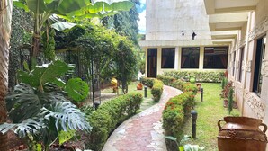 A garden pathway with potted plants and a tiled walkway leading to a building with large windows.