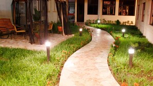 A pathway leading to a covered seating area with chairs and tables, surrounded by a garden with a stone path.