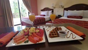 A hotel room with two beds, a dining table with breakfast, and a balcony with curtains.