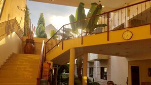 A spacious lobby with a staircase, a sofa set, and a large potted plant.