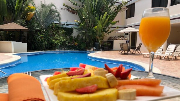 A poolside table with a fruit platter, a rolled towel, and a glass of orange juice.