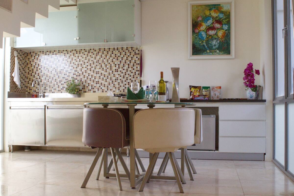 A modern kitchen with a tiled backsplash, a dining table with chairs, and a refrigerator.