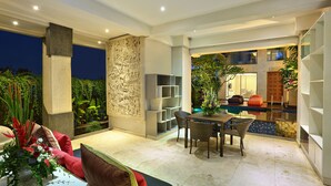 A spacious outdoor area with a dining table and chairs, surrounded by lush greenery and a decorative wall. - Echo Beach Resort (Canggu)