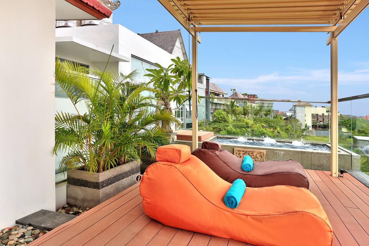A rooftop deck with three bean bags, a wooden pergola, and a view of buildings and greenery.
