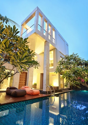 Un edificio moderno con piscina, ventanas amplias y mobiliario exterior.