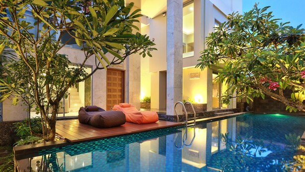 An indoor infinity pool with a wooden deck, lounge chairs, and lush greenery. - Echo Beach Resort (Canggu)