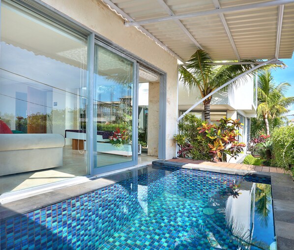 A modern pool area with a glass enclosure, a covered patio, and lush tropical plants.