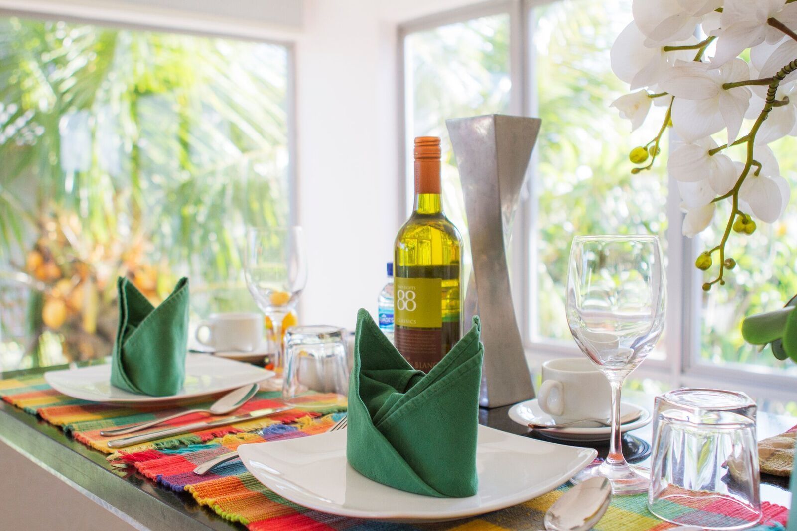 A dining table set with green napkins, a bottle of wine, and a vase of white flowers.
