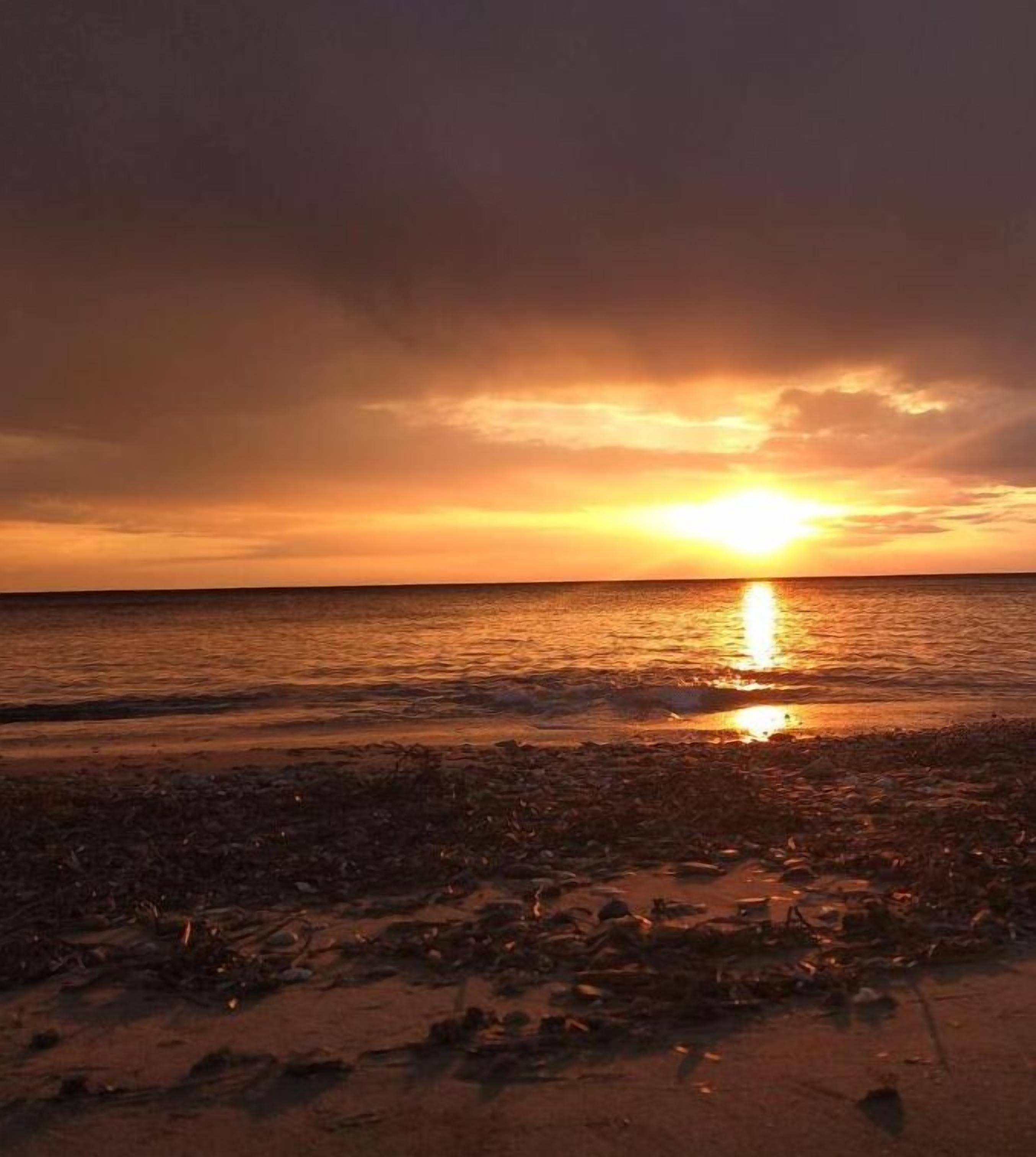 A beach at sunset with the sun reflecting on the water.