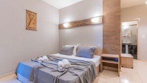 En pænt redt seng med gråt og blåt sengetæppe, et træhovedgærde og et natbord med en lampe.