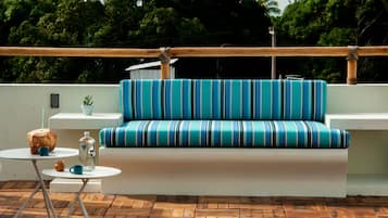 Et moderne udendørs loungeområde med en stribet sofa, et lille bord med en kokosdrik og en potteplante.