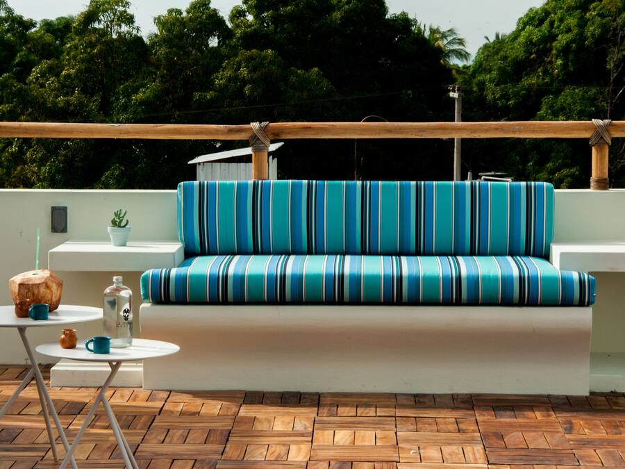 Et moderne udendørs loungeområde med en stribet sofa, et lille bord med en kokosdrik og en potteplante.
