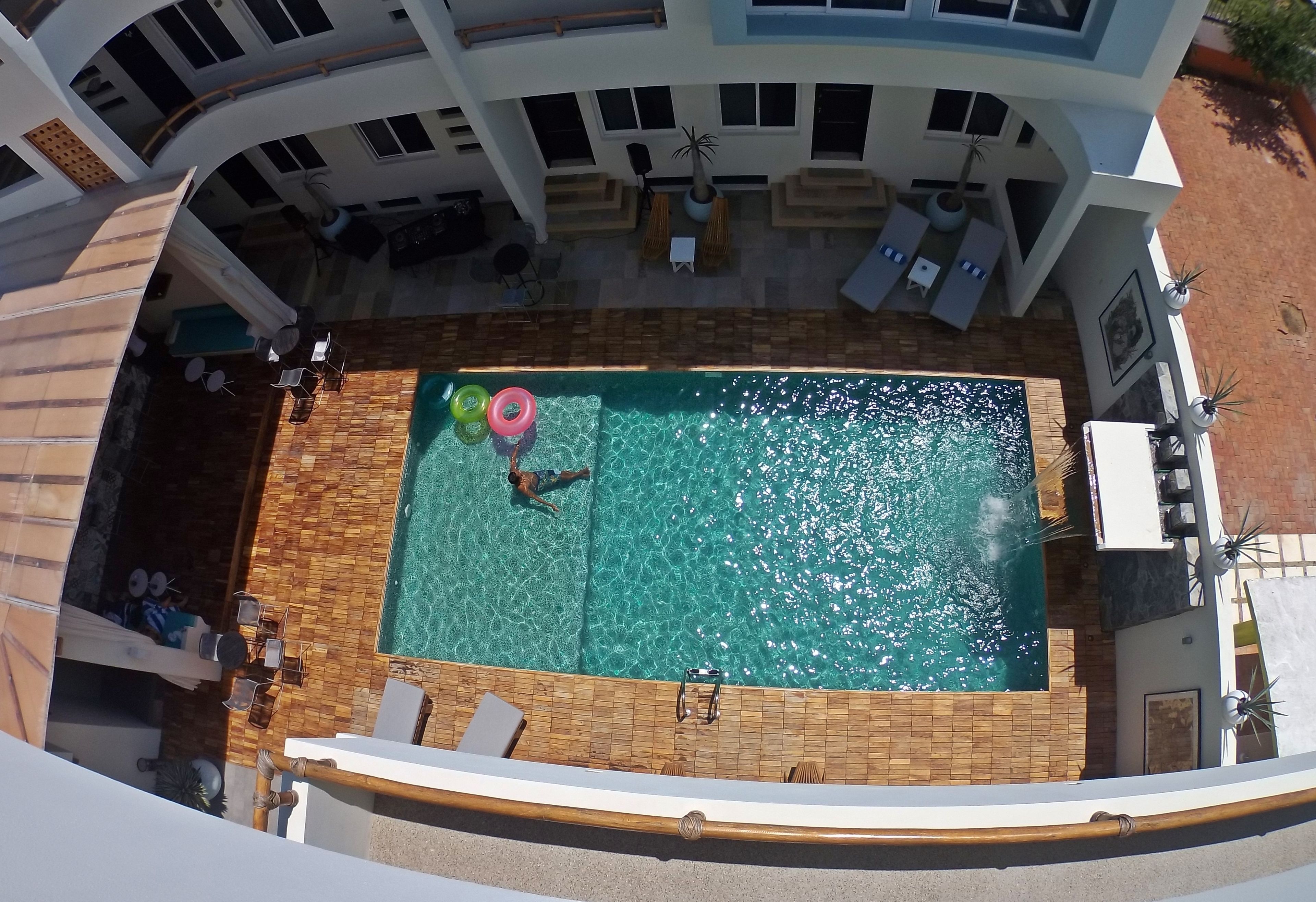 Vista aérea de una piscina rodeada por un porche cubierto con sillas de descanso y un conjunto de mobiliario.