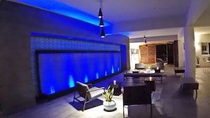 Una sala de estar moderna con una pared iluminada en azul, un sofá, una mesa de centro y un candelabro colgante.