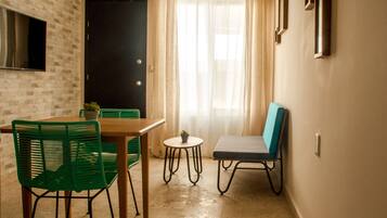 Un pequeño comedor con una mesa y sillas, una planta en maceta y vistas de una puerta y una ventana con cortinas.
